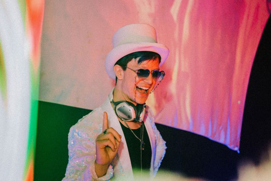 chillbill smiling behind the decks in a white top hat and sequin jacket