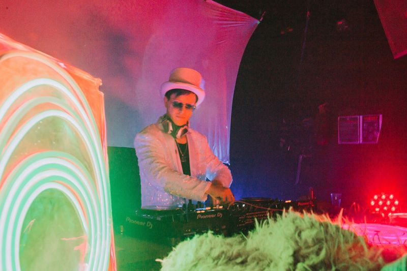 chillbill in a white top hat at the decks beside a glowing neon ring sculpture