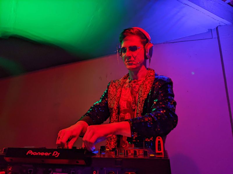 chillbill in a black sequin jacket mixing under green and magenta light
