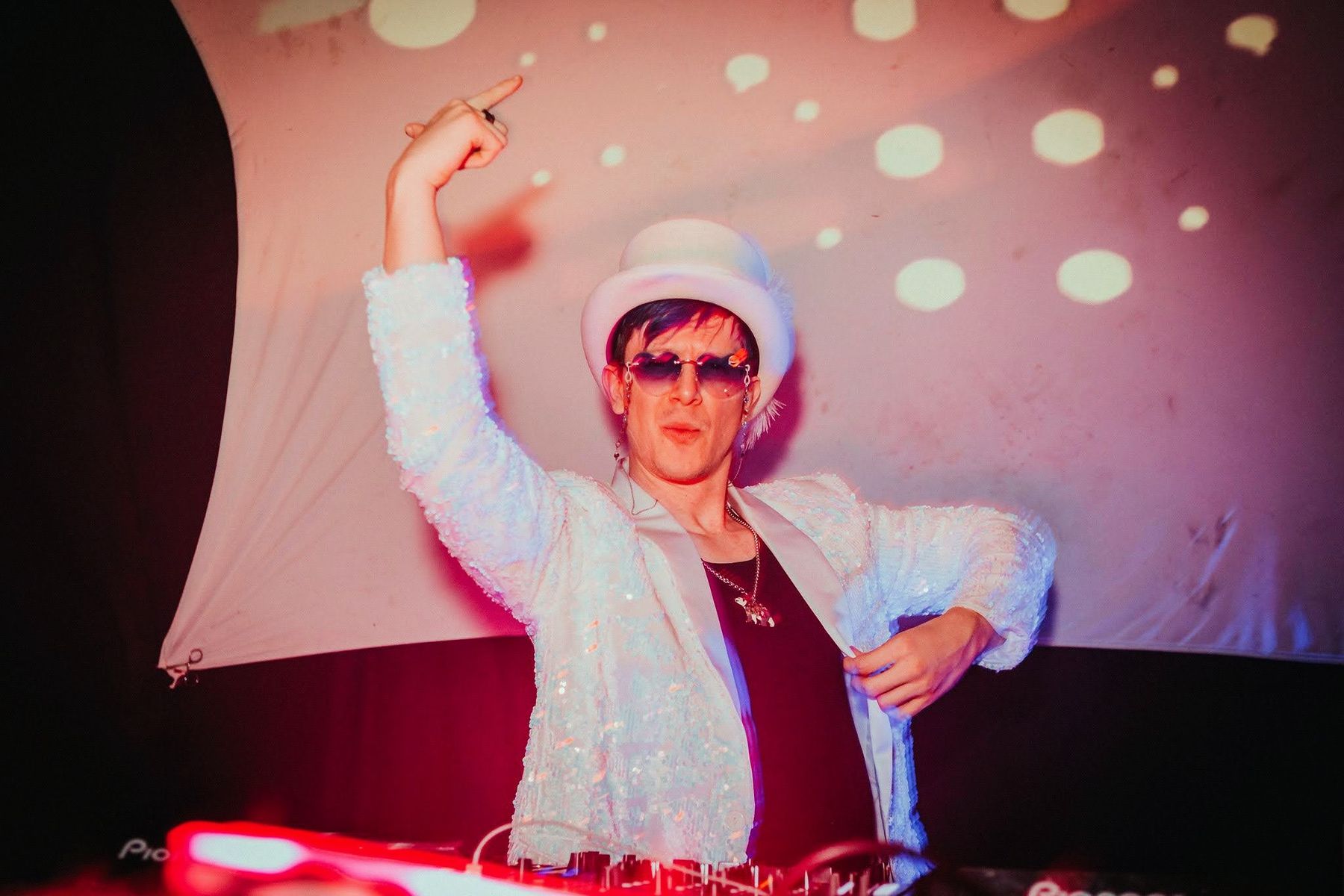 chillbill mid-set in a white sequin jacket and top hat, one arm in the air